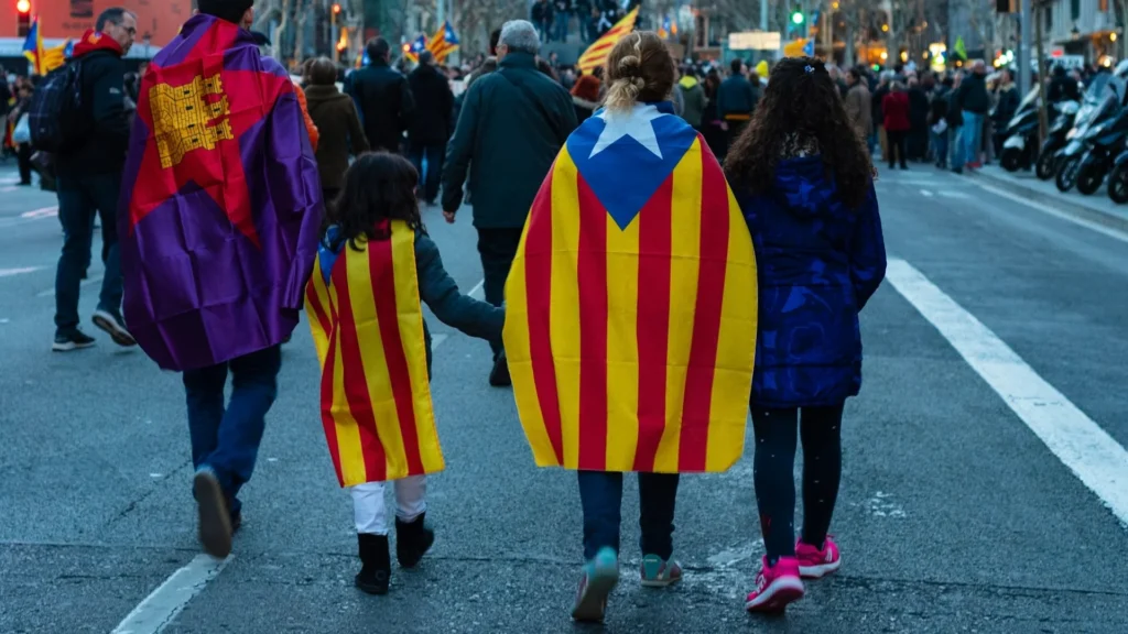 Компания людей с флагами Каталонии идут по улице