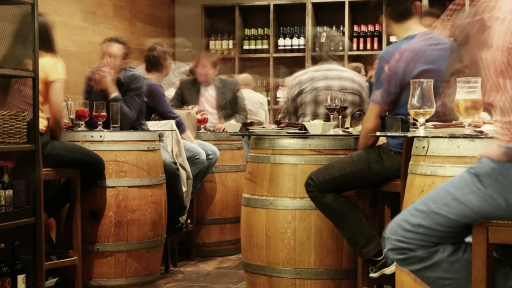 Люди разных возрастов в баре за столиками в виде бочек