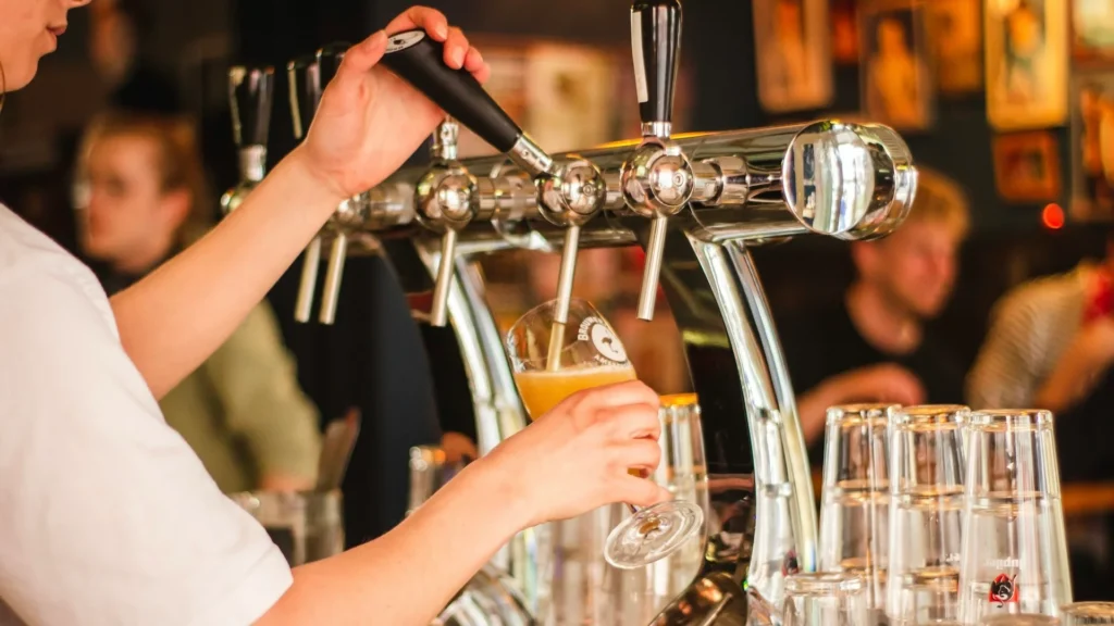 Бармен наливает пиво в стакан; на фоне много людей