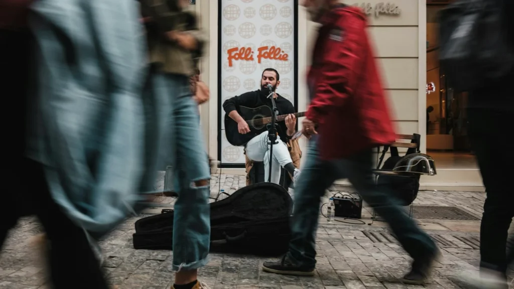 Уличный музыкант играет на гитаре на фоне идущих мимо людей