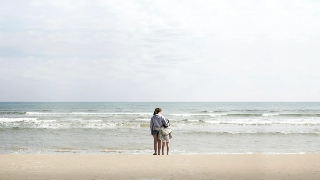 Мать с ребенком стоят у моря на пляже