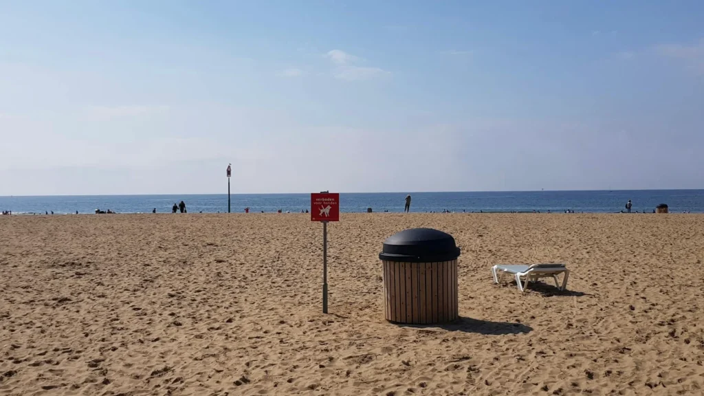 Мусорный бак и предупреждающий знак на пляже у моря