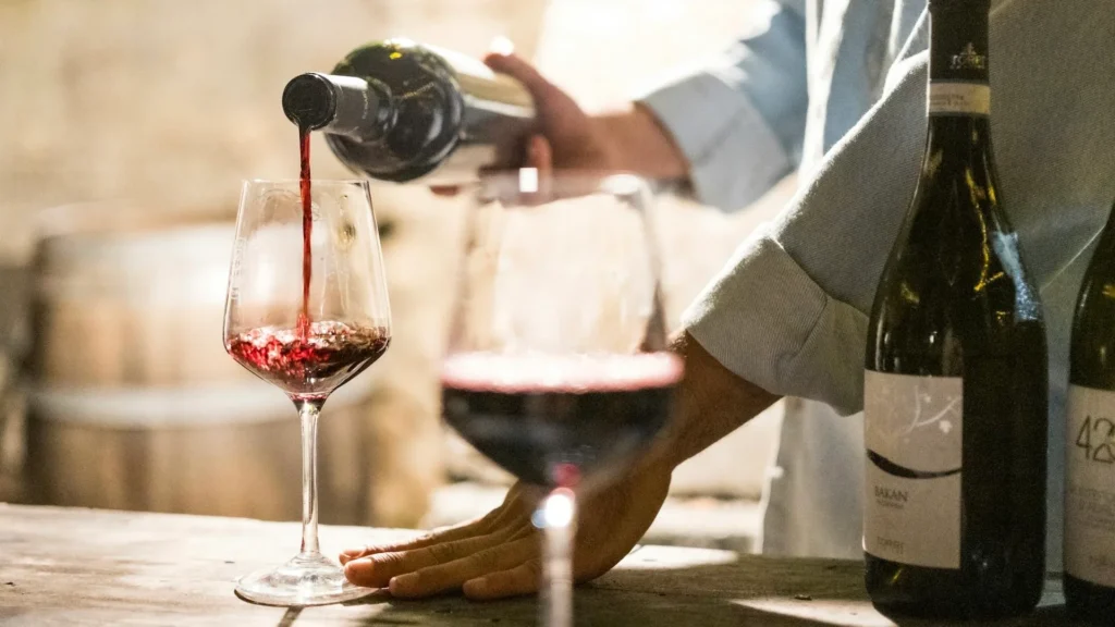 Мужчина наливает красное вино в бокал