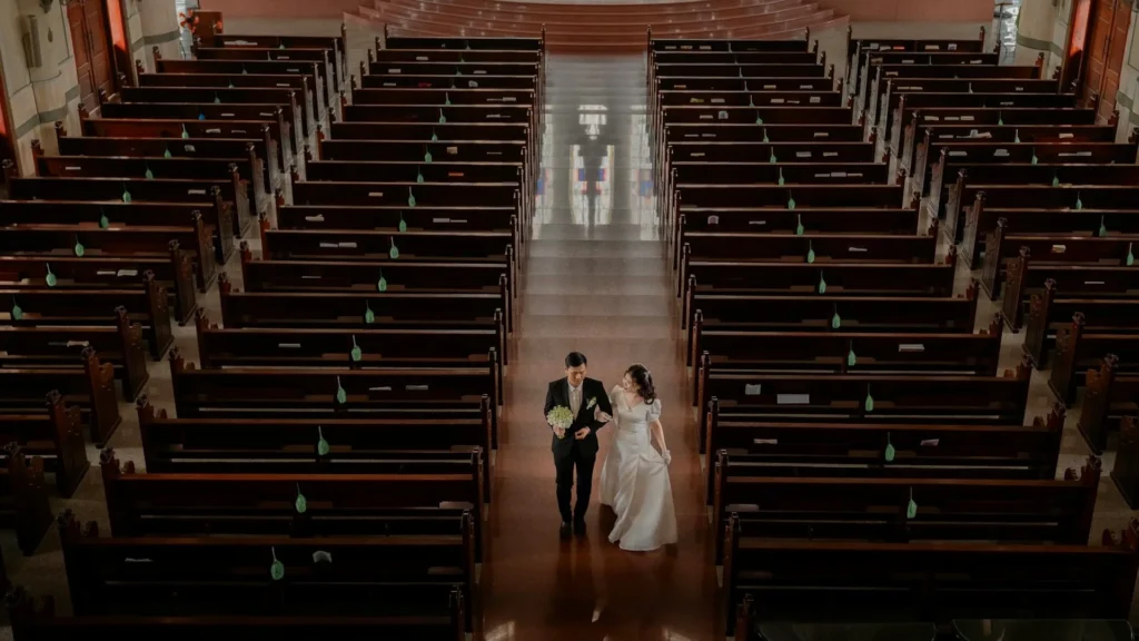 Пара молодоженов идет по проходу в церкви между скамейками