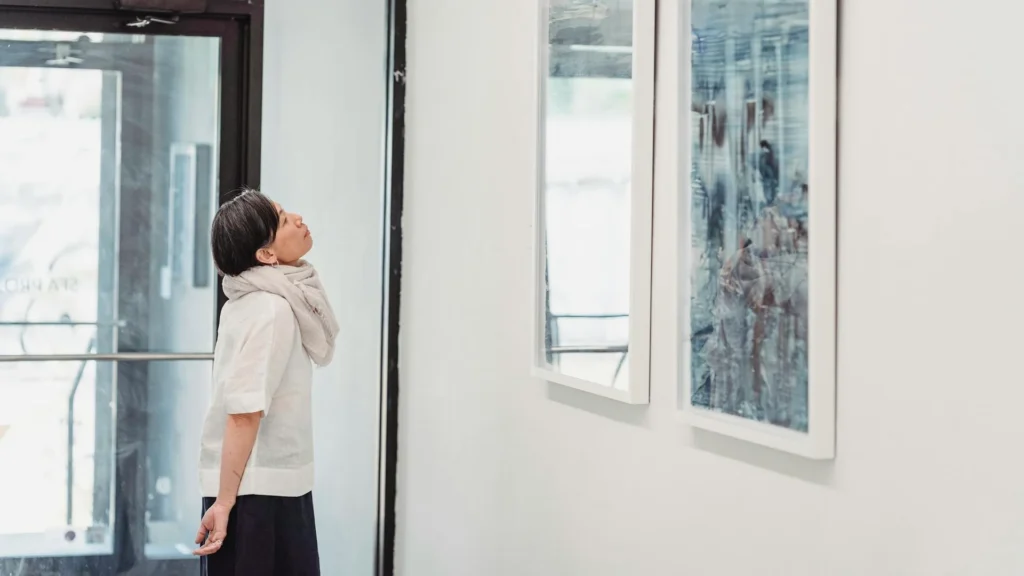 Жензина смотрит на картину в помещении с белыми стенами