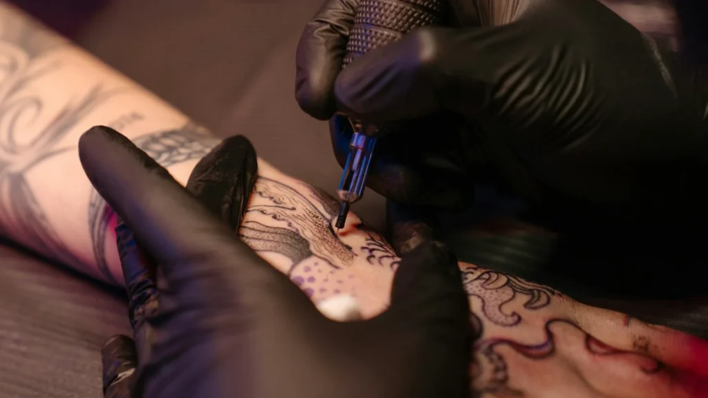 Тату-мастер делает татуировку на руке клиенту