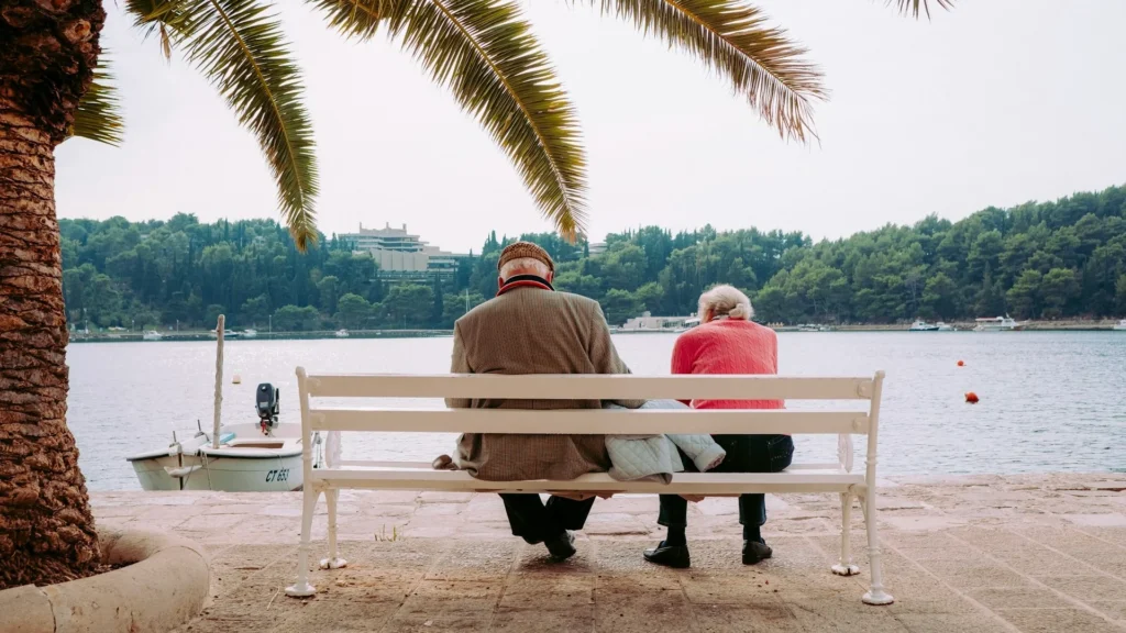 пара пенсионеров сидит на лавочке и смотрит на озеро