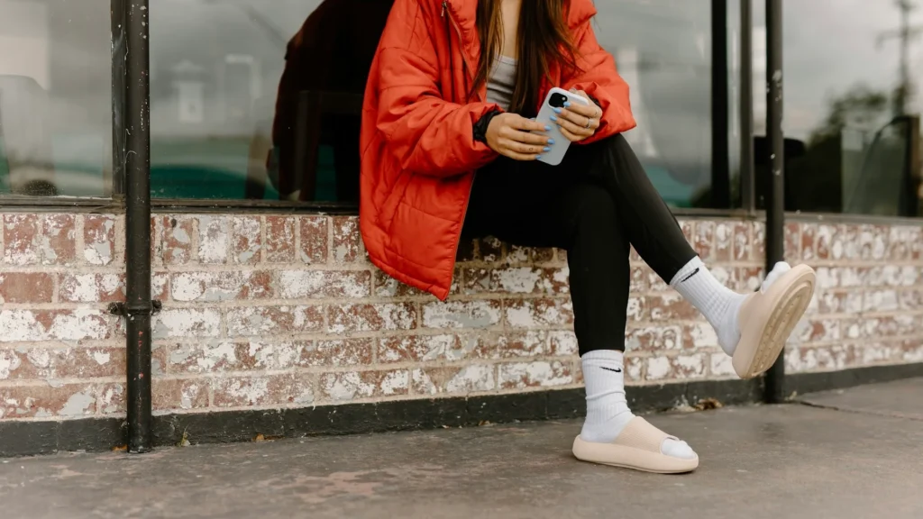 Днвушка в яркой куртке сидит на парапете с телефоном в руках