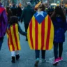 Компания людей с флагами Каталонии идут по улице