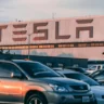 Автомобили на стоянке на фоне вывески Tesla