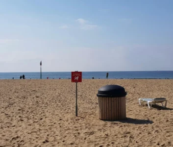 Мусорный бак и предупреждающий знак на пляже у моря